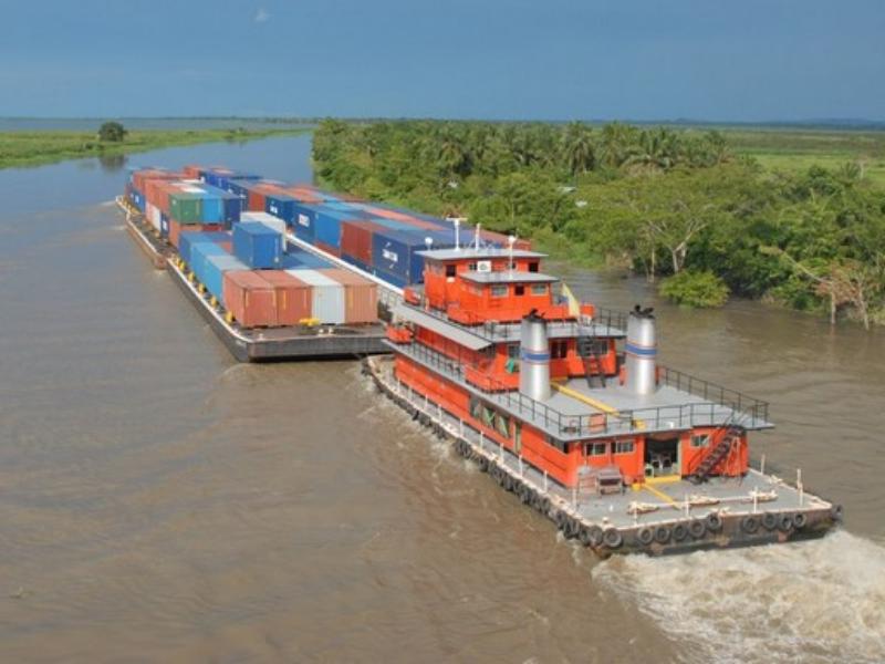 Barco empurrador transportando barcaças com contêineres no rio Amazonas, cercado por vegetação ribeirinha