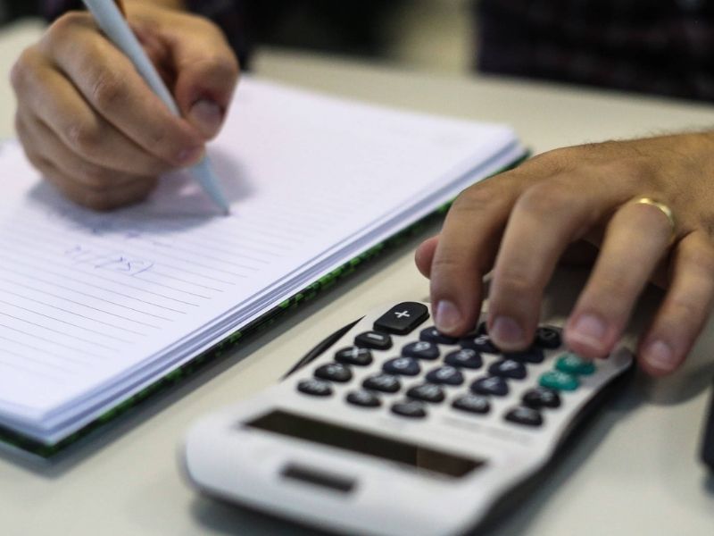 Pessoa fazendo contas em caderno com calculadora ao lado representa adesão ao Refis 2025