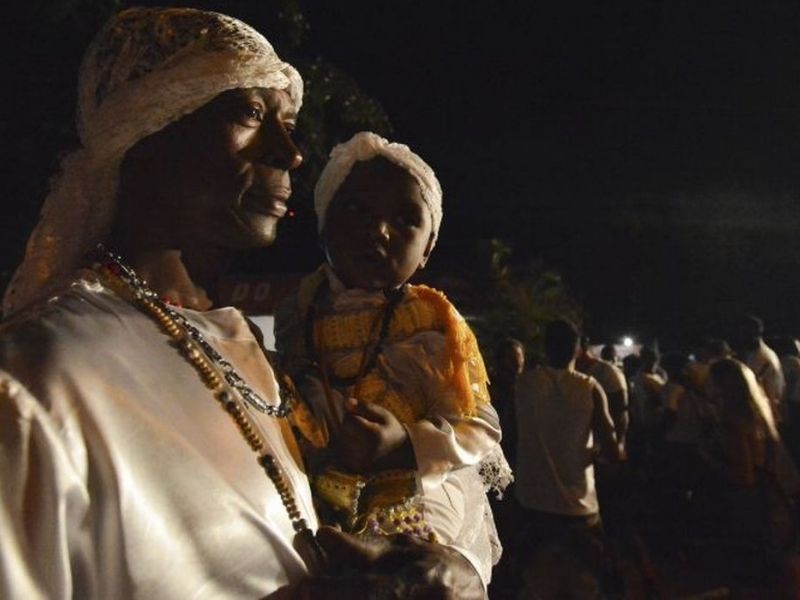 Pessoa adulta e criança vestidas com roupas tradicionais de matriz africana durante atividade cultural noturna.