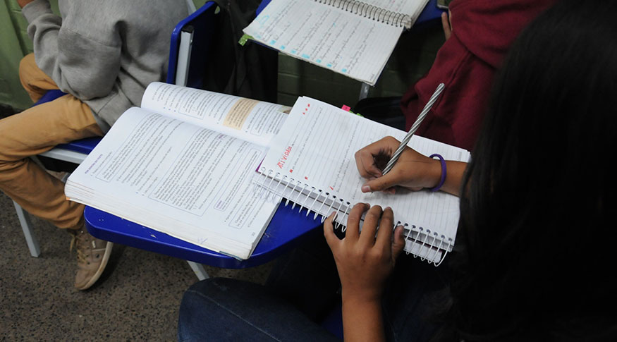 Estudante escreve em caderno em sala de aula do amazonas
