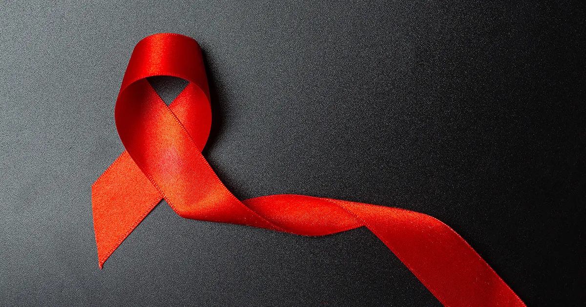 Fita vermelha dobrada em laço sobre fundo preto, símbolo do combate ao HIV/Aids