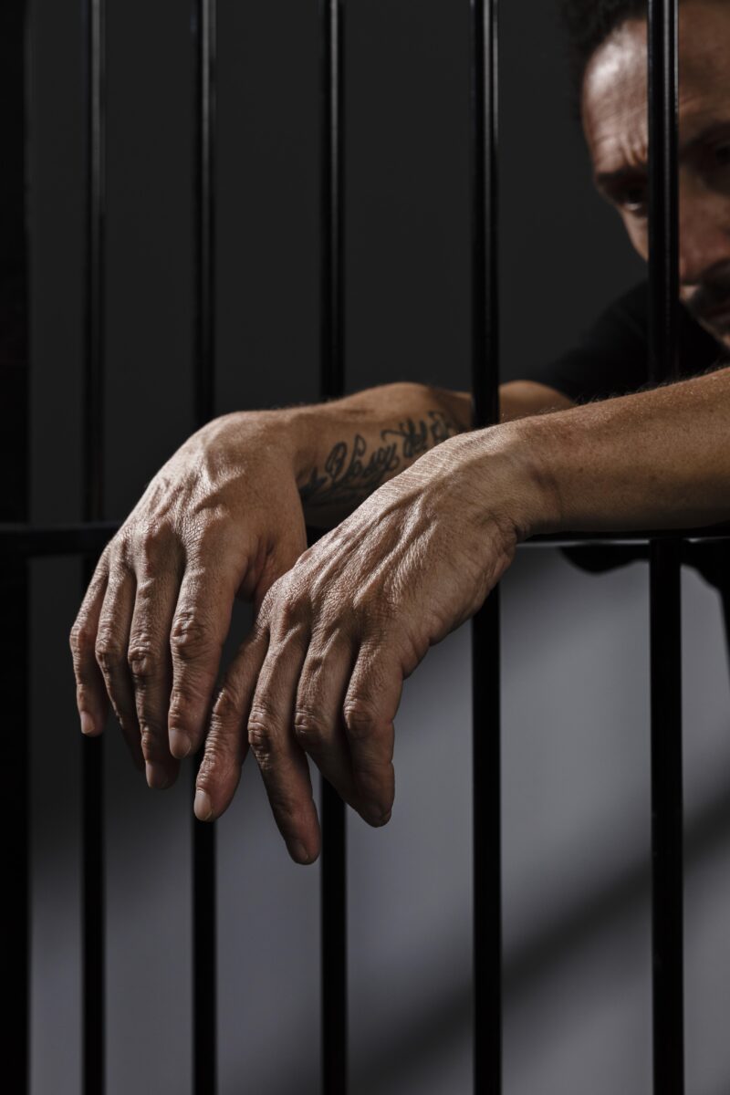 Imagem das mãos de um homem atrás das grades/Homem preso