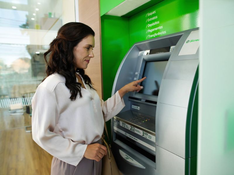 Mulher acessa caixa eletrônico em agência bancária para consultar saldo e realizar operações