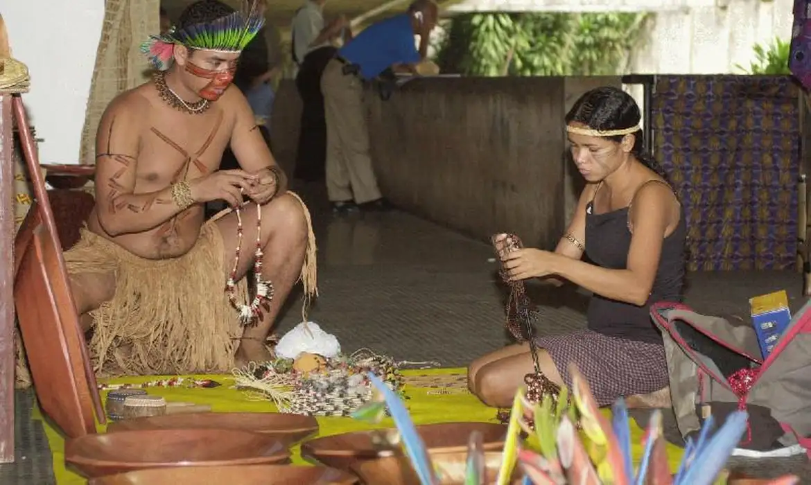índios em uma oca produzindo artezanato