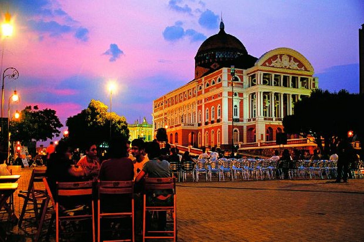 Teatro Amazonas ao entardecer com pessoas reunidas na Praça São Sebastião, em Manaus.
