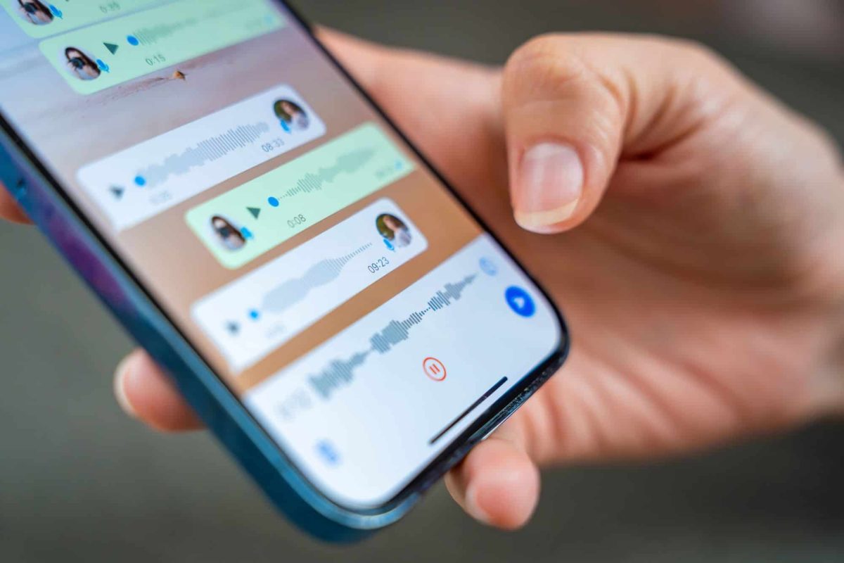 Pessoa segura celular exibindo tela com áudios de voz em aplicativo de mensagens.