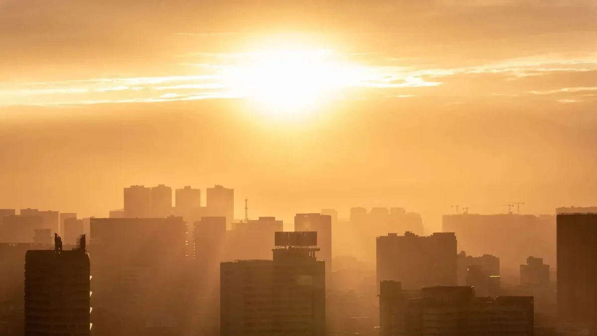 Sol forte iluminando prédios de uma grande cidade sob calor extremo e atmosfera amarelada.