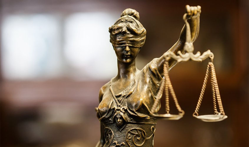 Estátua de bronze da deusa Têmis segurando uma balança da justiça com fundo desfocado.