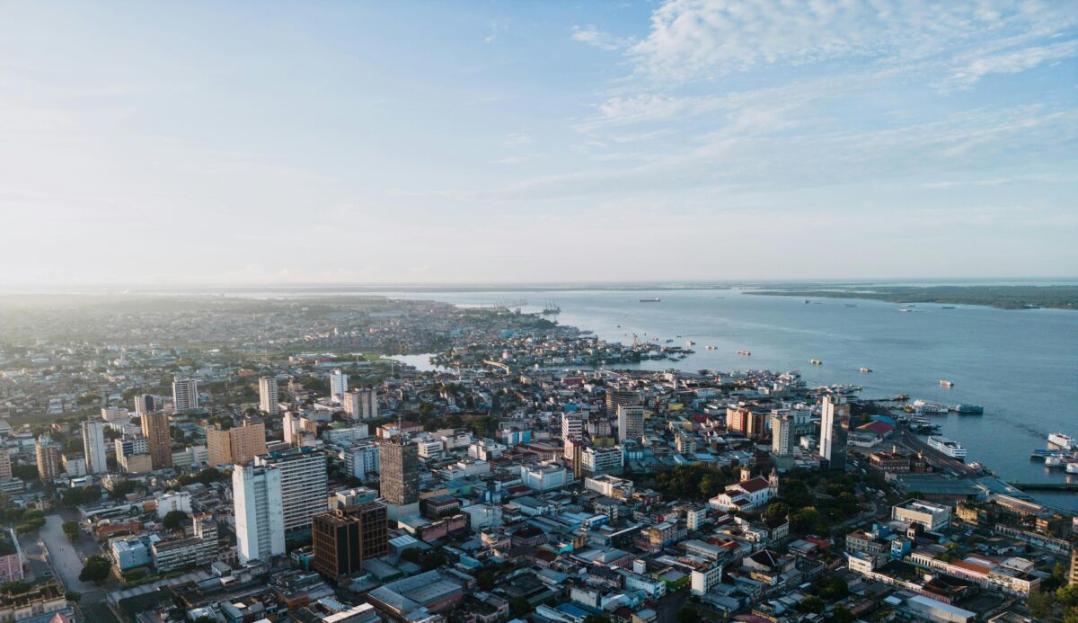 Vista aérea de Manaus com o Rio Negro ao fundo, mostrando prédios, porto e área central da cidade.