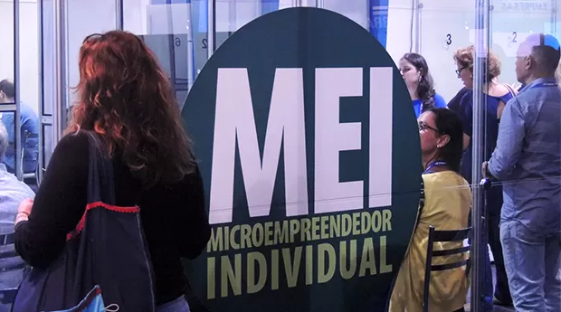 Pessoas em fila de atendimento diante de painel do Microempreendedor Individual, MEI