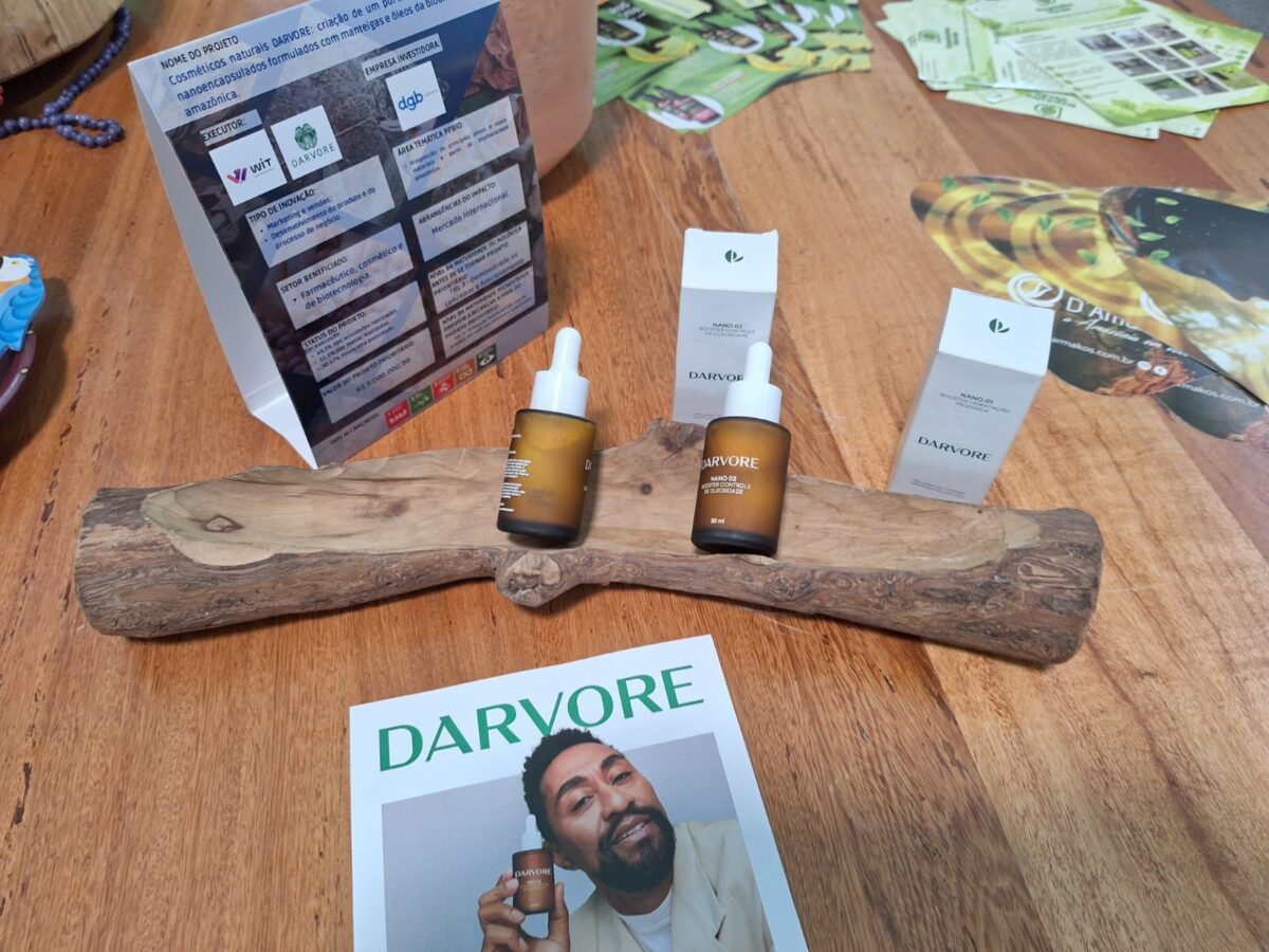 Dois frascos dos cosméticos D’Arvore sobre base de madeira, ao lado das caixas e material de divulgação da marca, que utiliza tecnologia de nanoencapsulamento com ativos amazônicos.