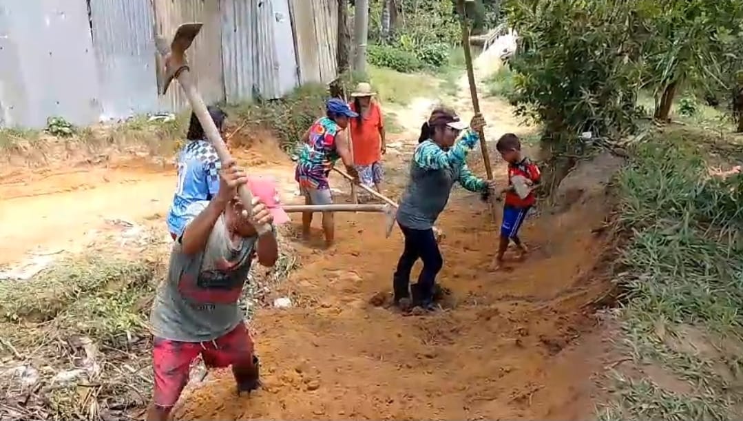 Moradores da Comunidade Nossa Senhora do Livramento, incluindo adultos e crianças, trabalham com enxadas e pás para recuperar uma rua de terra durante mutirão iniciado em 22 de outubro.