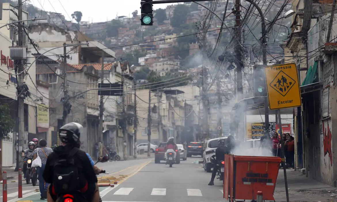 Motociclistas circulam por rua com fumaça após confronto policial no Complexo da Penha, no Rio de Janeiro.