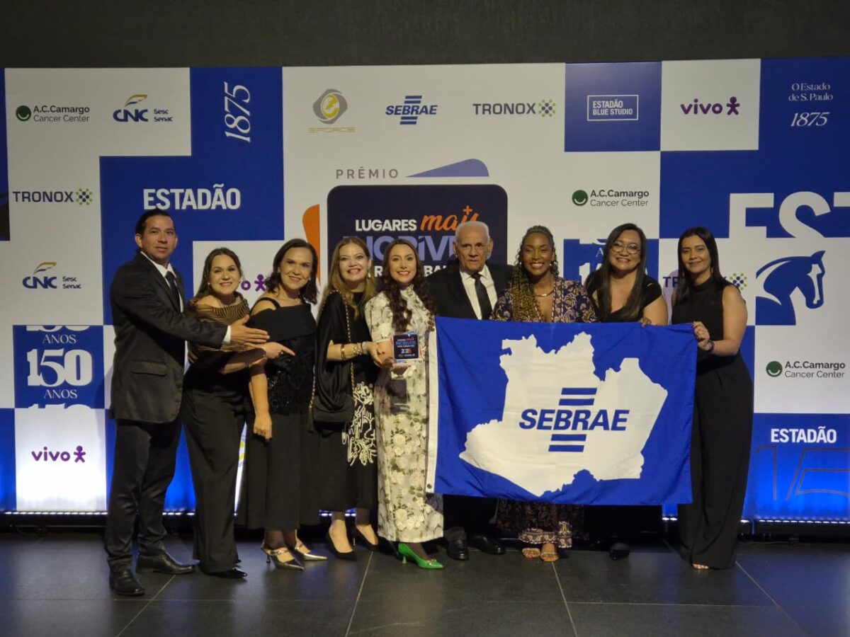 Grupo de colaboradores do Sebrae Amazonas posa sorridente segurando uma bandeira da instituição durante a premiação nacional em São Paulo.