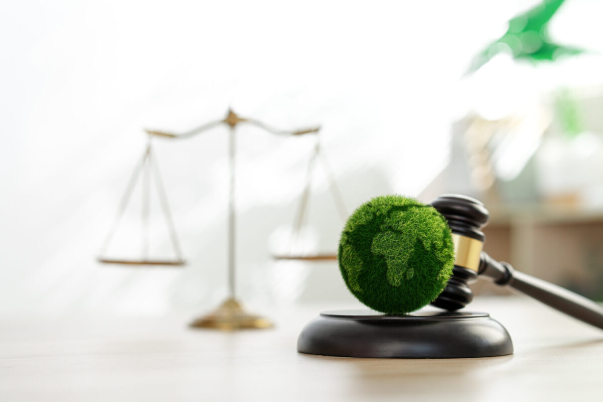 Martelo de juiz com globo verde simbolizando sustentabilidade e justiça ambiental, com balança ao fundo.