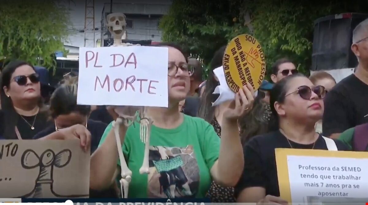 Professores protestam em Manaus contra a reforma da previdência municipal segurando cartazes e um boneco simbolizando o “PL da Morte”.