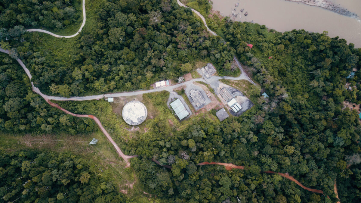 Vista aérea de uma área de floresta amazônica com pequenas construções e estradas de acesso, mostrando a integração entre infraestrutura e natureza, símbolo da economia da floresta que ganha força fora dos espaços oficiais da COP30 em Belém.