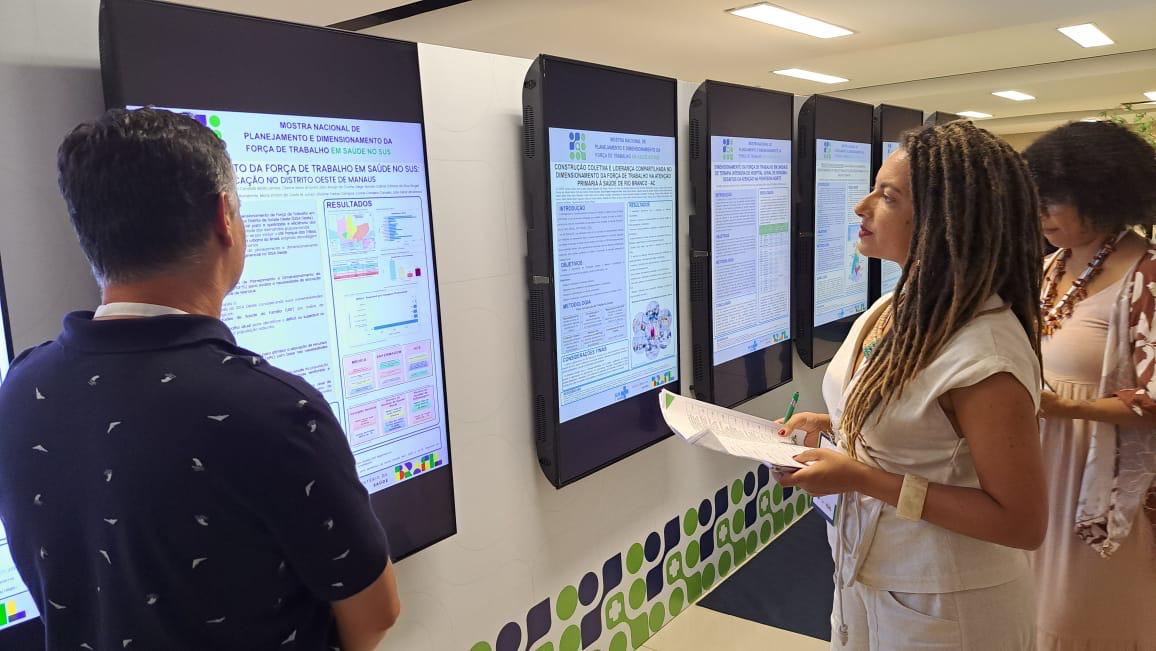 Servidores observam painéis digitais com projetos apresentados na Mostra Nacional de Planejamento em Saúde, em Brasília.