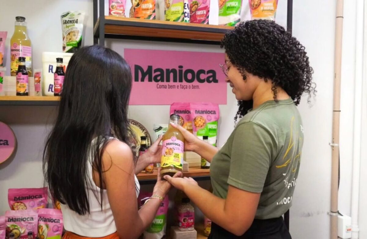 Duas mulheres observam produtos da Manioca em uma prateleira durante roteiro turístico da COP30.