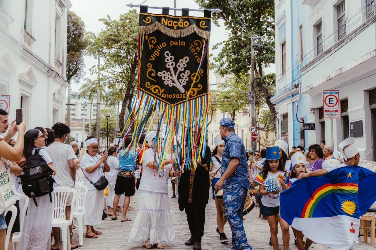 Lideranças religiosas, artistas e participantes seguram o estandarte “Nação – Vigília pela Terra 2025” durante ato inter-religioso em Belém, com fitas coloridas e trajes tradicionais.