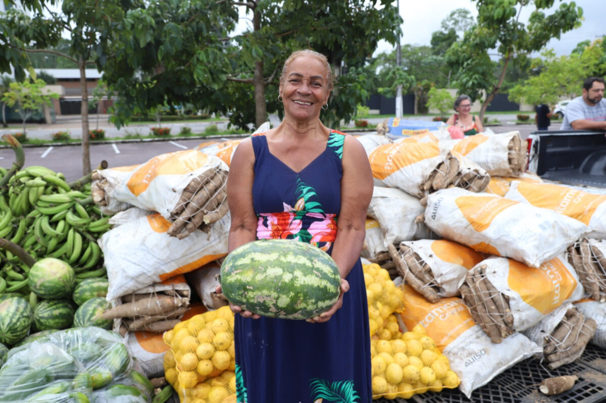 Agricultora familiar segura melancia em frente a sacas de alimentos adquiridos pelo PAA no Amazonas.