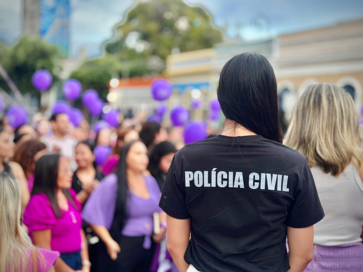 Agente da Polícia Civil do Amazonas observa manifestação com mulheres segurando balões roxos em ato contra a violência doméstica.