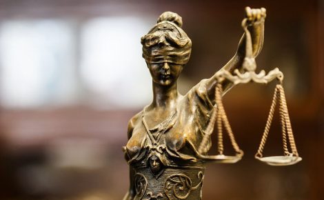 Estátua de bronze da deusa Têmis segurando uma balança da justiça com fundo desfocado.