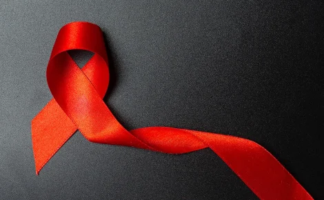 Fita vermelha dobrada em laço sobre fundo preto, símbolo do combate ao HIV/Aids