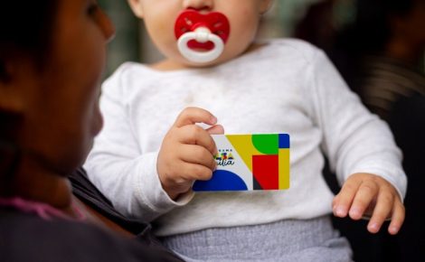 Criança segurando cartão do Bolsa Família no colo da mãe. (Foto: Gov.br)