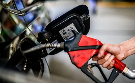 Pessoa abastece veículo em posto de combustíveis com bomba de gasolina vermelha.