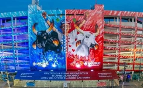 Fachada iluminada do Bumbódromo de Parintins exibe grandes murais dos bois Caprichoso e Garantido, com luzes azul e vermelha representando cada lado da arena.