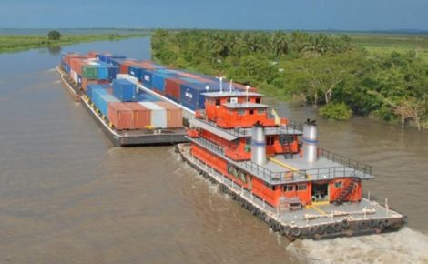 Barco empurrador transportando barcaças com contêineres no rio Amazonas, cercado por vegetação ribeirinha
