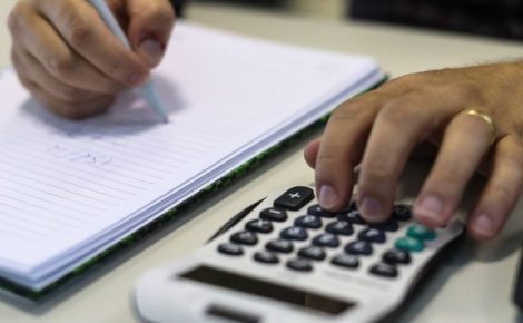 Pessoa fazendo contas em caderno com calculadora ao lado representa adesão ao Refis 2025