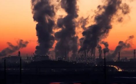Fumaça densa sai de chaminés industriais durante o pôr do sol, simbolizando o impacto humano nas mudanças climáticas