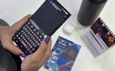 Pessoa usando o WhatsApp no celular para acessar o atendimento da Águas de Manaus, com panfleto da campanha Zera Dívida sobre a mesa.