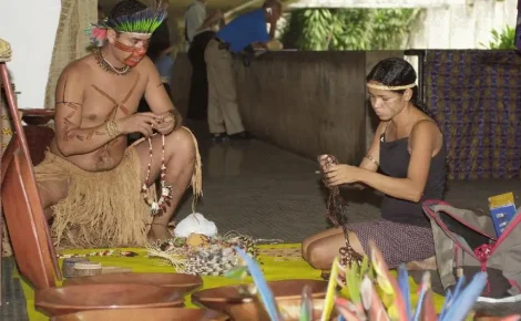 índios em uma oca produzindo artezanato