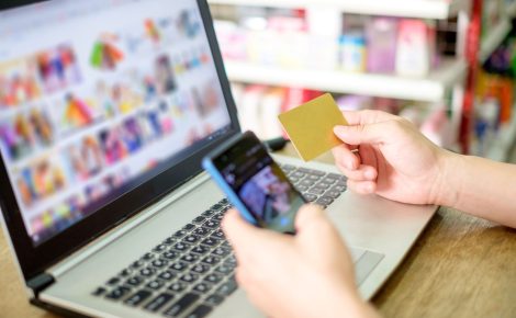 Pessoa utiliza notebook e smartphone para comprar online com cartão em mãos.