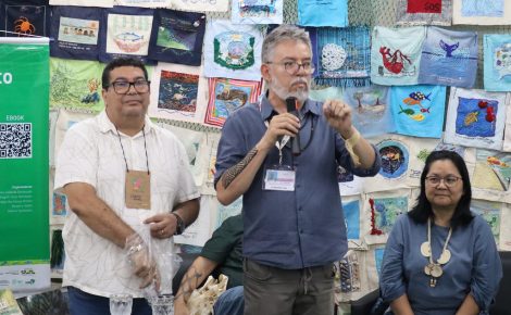 Três participantes falam ao público durante lançamento de livros do Inpa na COP30, diante de painel com trabalhos têxteis.