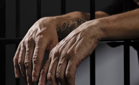 Imagem das mãos de um homem atrás das grades/Homem preso