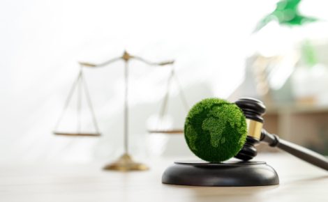 Martelo de juiz com globo verde simbolizando sustentabilidade e justiça ambiental, com balança ao fundo.