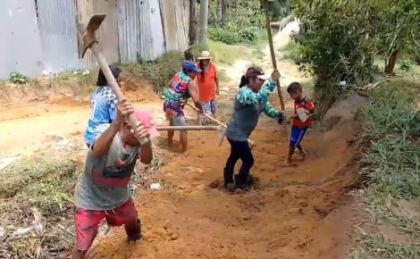 Moradores da Comunidade Nossa Senhora do Livramento, incluindo adultos e crianças, trabalham com enxadas e pás para recuperar uma rua de terra durante mutirão iniciado em 22 de outubro.