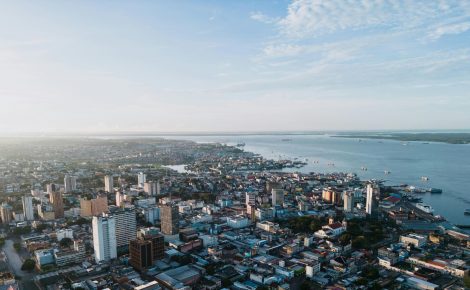 Vista aérea de Manaus com o Rio Negro ao fundo, mostrando prédios, porto e área central da cidade.