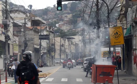 Motociclistas circulam por rua com fumaça após confronto policial no Complexo da Penha, no Rio de Janeiro.