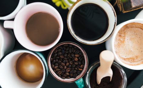 multiple coffee cups, milk, beans and ground coffee in jar on black background