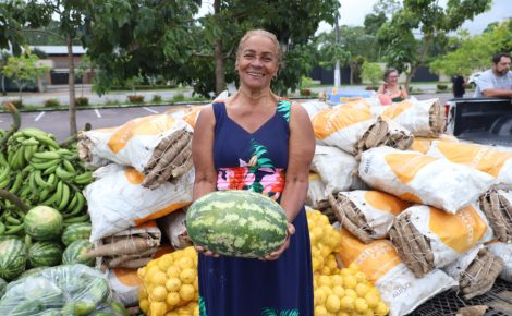 Agricultora familiar segura melancia em frente a sacas de alimentos adquiridos pelo PAA no Amazonas.