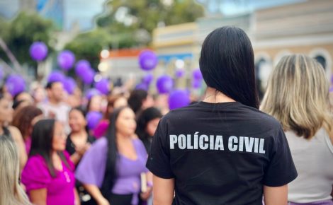 Agente da Polícia Civil do Amazonas observa manifestação com mulheres segurando balões roxos em ato contra a violência doméstica.