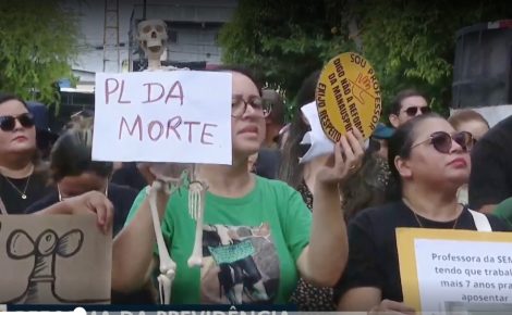 Professores protestam em Manaus contra a reforma da previdência municipal segurando cartazes e um boneco simbolizando o “PL da Morte”.