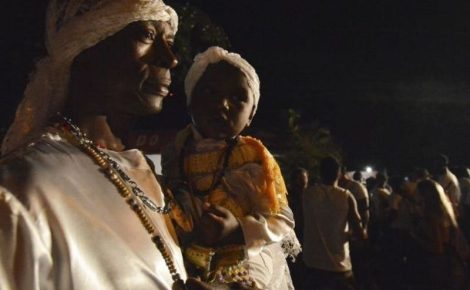 Pessoa adulta e criança vestidas com roupas tradicionais de matriz africana durante atividade cultural noturna.