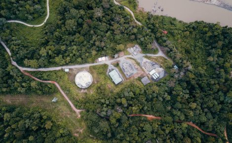 Vista aérea de uma área de floresta amazônica com pequenas construções e estradas de acesso, mostrando a integração entre infraestrutura e natureza, símbolo da economia da floresta que ganha força fora dos espaços oficiais da COP30 em Belém.